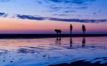Man en vrouw laten de hond uit op het strand bijzonsondergang van Marcel van den Bos