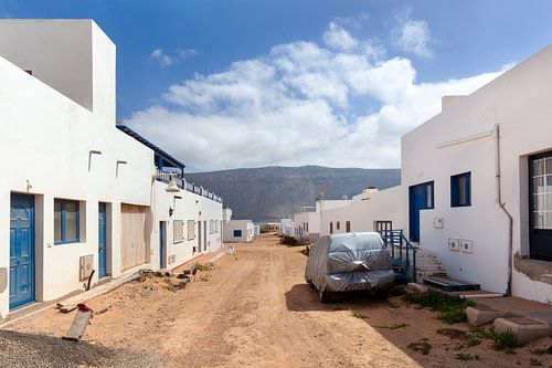 Rue vide avec du sable et des maisons blanches et une voiture enveloppée dans du plastique contre le