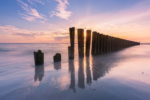 Paaltjes op het strand met ondergaande zon op Ameland