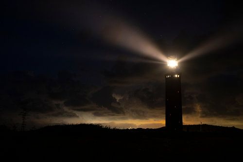 Vuurtoren in de duinen met lichtbundels bij nacht