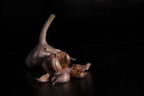 a still life with a whole fresh garlic and garlic cloves on a black background with reflection