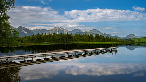 Het Hopfensee met de weerspiegeling van de bergen en een steiger tegen de achtergrond van het Alpenpanorama