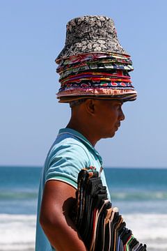 Beach vendor with pile of hats by Anne Ponsen