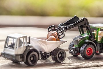 A toy tractor loads a toy truck with a babe by Annabell Gsödl