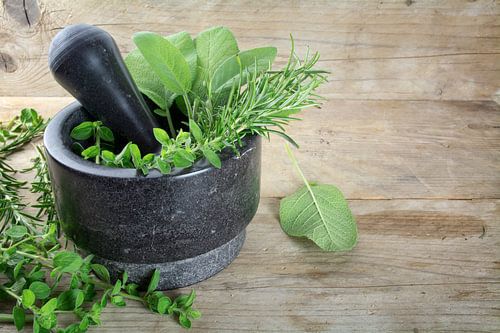 fresh Mediterranean herbs, oregano, rosemary and sage in a mortar made of black granite on a rustic 