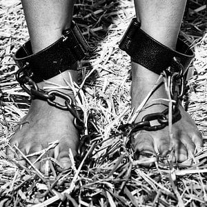 Pieds et jambes de femmes entravés par de lourdes chaînes de cachot.