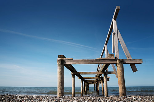 Zerbrochener hölzerner Pier oder Steg führt ins Meer vor blauem Himmel, Perspektive von unten, Kopie