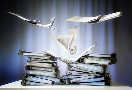 fliegende Ringbücher mit Akten und Dokumenten landen auf Stapeln auf einem Büroschreibtisch, Konzept