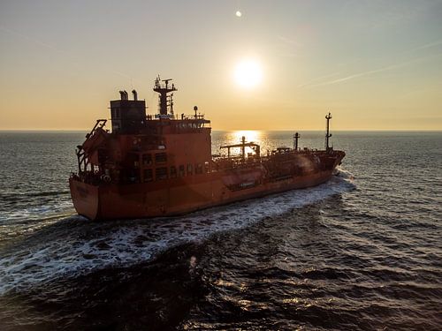 Een eenzame boot drijft stil onder een vurige hemel – een zonsondergang gevangen in vogelvlucht boven het kalme water van een gouden avond