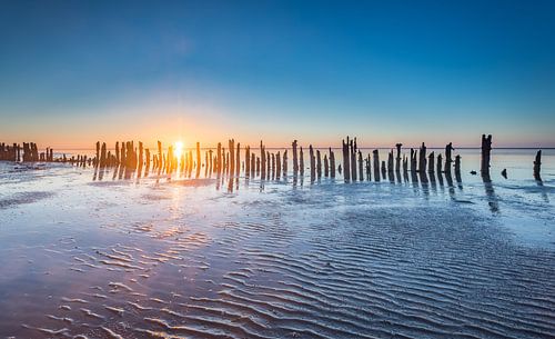 Paaltjes aan de Waddenzee tijdens zonsondergang
