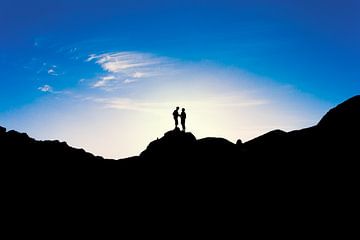 Silhouetten van twee mensen die op de top van een berg staan bij zonsondergang. Wout Kok One2expose van Wout Kok