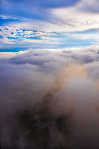 Beautiful clouds below swirl, illuminated pink and orange from the setting sun, on top of the blue s