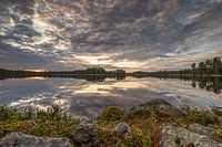 Stones and heather on a mirror-smooth Swedish lake under an imposing cloud cover