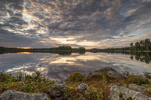Stones and heather on a mirror-smooth Swedish lake under an imposing cloud cover