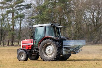 Rode tractor op een weiland met een kalkspreider in het vroege voorjaar in Nederland