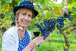 Frau mittleren Alters im Weinberg zeigt blauen Trauben mit Weinglas