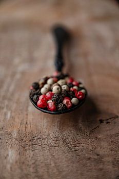 Peppercorns on a black spoon and Walnut wood
