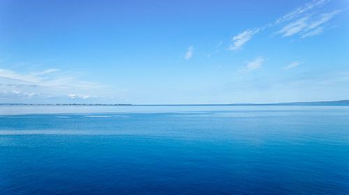 Een rustig zeegezicht onder een heldere hemel. Het water weerspiegelt zachte wolken.