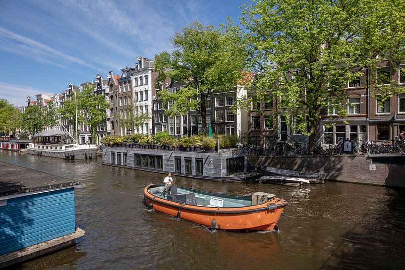 Canal in Amsterdam with orange sloop. by Joost Adriaanse
