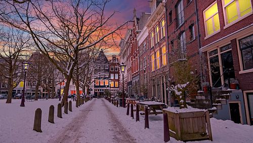 Stadsbeeld van Amsterdam in de sneeuw bij zonsondergang in Nederland