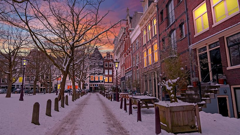 Stadsbeeld van Amsterdam in de sneeuw bij zonsondergang in Nederland van Eye on You