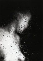 Naked young woman behind a window with raindrops.
