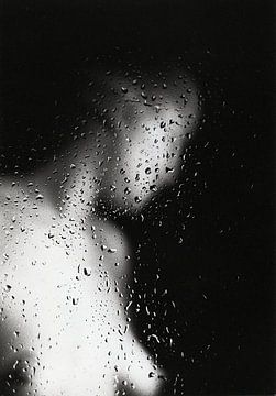 Naakte jonge vrouw achter een raam met regen druppels.