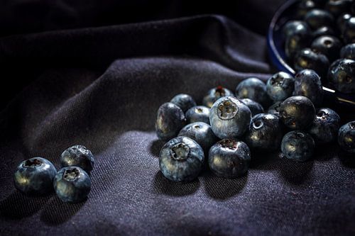 Ripe blueberries rolling on a dark purple napkin, dark and moody