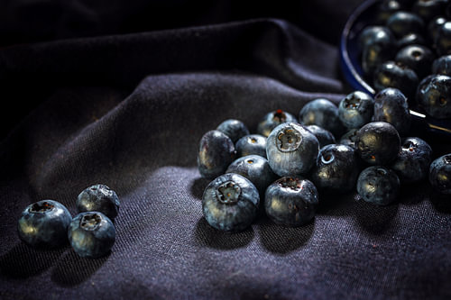 Reife Blaubeeren rollen auf einer dunkelvioletten Serviette, dunkel und stimmungsvoll