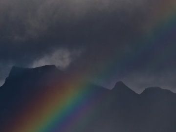 Strong, colorful rainbow in front of rugged mountains by Timon Schneider