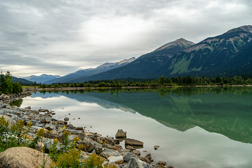 Moose Lake mit Steinen und Pflanzen im Vordergrund und Bergen und Himmel im Hintergrund