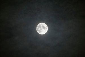 Full moon shining through the clouds in the dark night sky