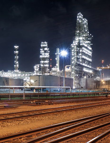 Train rails and illuminated petrochemical industry at nighttime by Tony Vingerhoets