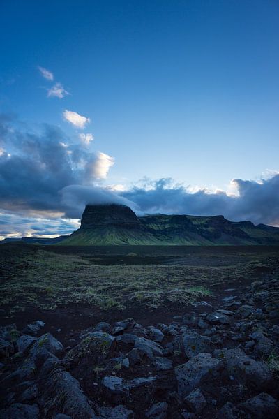 Iceland - Glowing clouds hanging over green mountain behind lava fields by adventure-photos