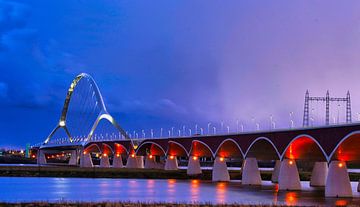 De oversteek, brug bij Nijmegen in avondlicht. van Machiel Zwarts