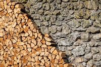 Pile de bois de chauffage devant un mur en pierre naturelle