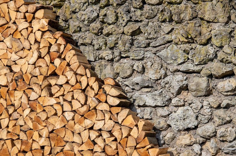 Pile de bois de chauffage devant un mur en pierre naturelle par Fartifos