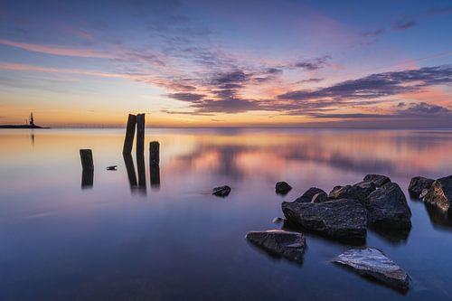 Nederlands kustlandschap bij zonsopkomst met stenen oever en houten palen in het IJsselmeer