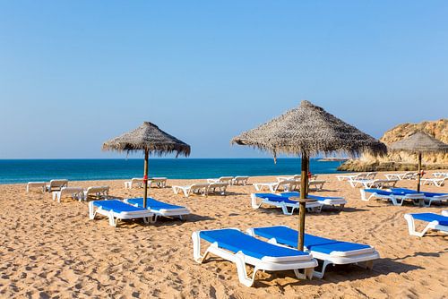 Groep rieten parasols en blauwe ligbedden op strand in Albufeira Portugal