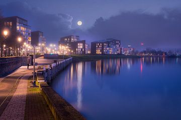 De pothoofd in Deventer met gebouwen aan de rivier en de maand tussen de wolken