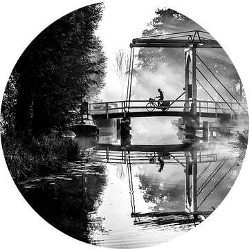 Eenzame krantenbezorger fietst over een brug in IJlst Friesland. One2expose Wout Kok Photography.  van Wout Kok