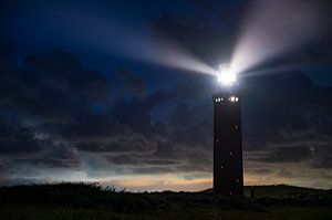 Leuchtturm in den Dünen mit Lichtstrahlen bei Nacht