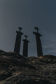 Wikinger-Geschichte – Vertikaler Fotodruck der drei „Sverd i fjell“-Schwerter bei Hafrsfjord bei Sonnenuntergang von Dylan Winter Visuals