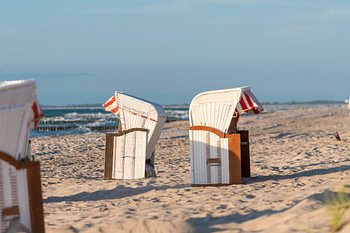 Strandstoelen staan in de zonsondergang op een badstrand aan de Oostzee met zee en heldere lucht.