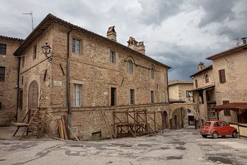 Red (Fiat 500) car in square in Bevagne, Italy by Joost Adriaanse