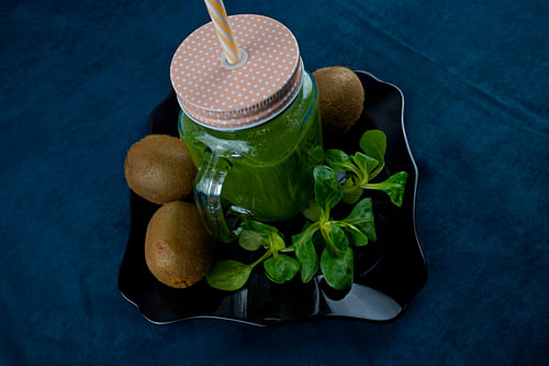 Bladsalade en kiwi smoothie op zwart bord versierd met kiwi