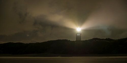 Vuurtoren in de duinen met lichtbundels bij nacht