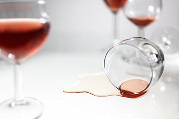 Verre renversé avec une flaque de vin rouge entre des verres flous, concept pour s'amuser en soirée, sur Maren Winter