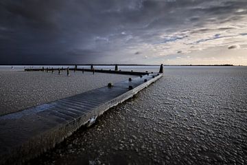 A cold sunrise in the winter above the Lauwersmeer. The water is frozen and the jetty covered with i