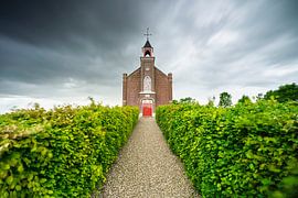 Kerkje onder dreigende wolken langs een groene laan